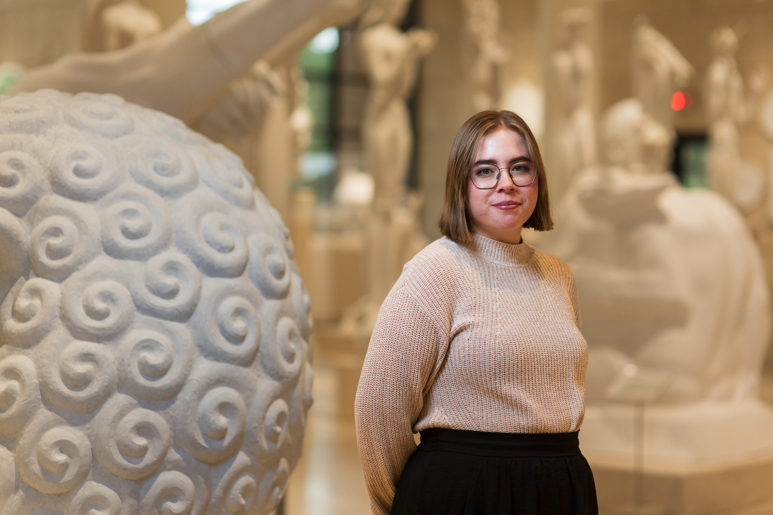 Woman in tan sweater standing next to sculpture